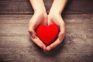 Hands holding a heart made out of red material.