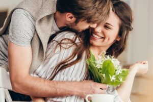 A happy man and woman hugging as the man gives the woman a bouquet of flowers.
